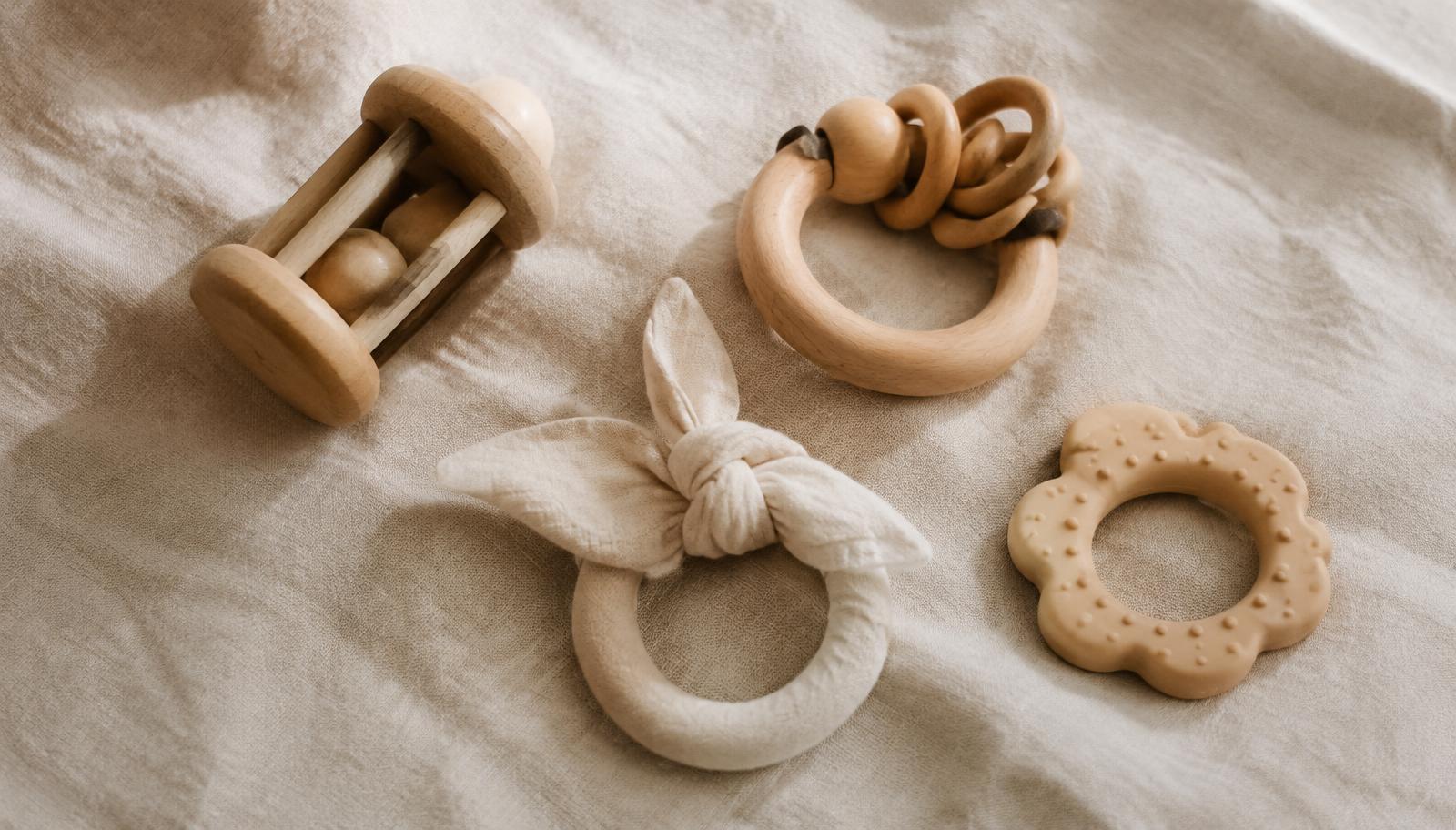 Wooden rattles, a cotton teether and a natural rubber teether on linen